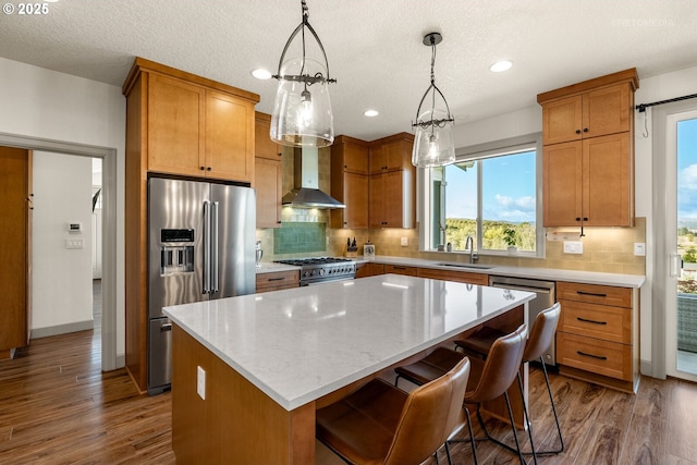 kitchen featuring high end appliances, wall chimney exhaust hood, decorative light fixtures, a center island, and a sink