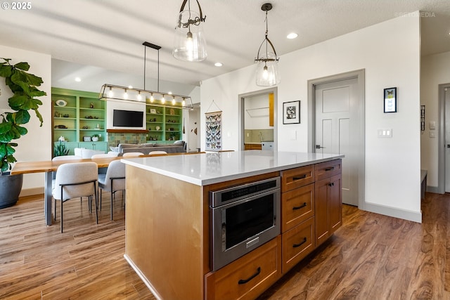 kitchen with wood finished floors, light countertops, a center island, brown cabinetry, and decorative light fixtures