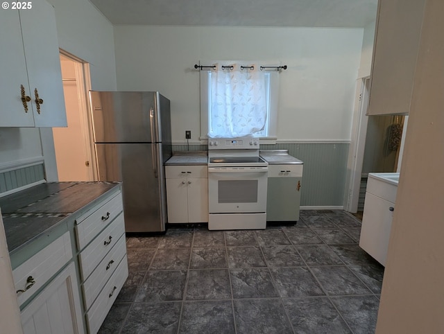 kitchen featuring a wainscoted wall, white electric range, freestanding refrigerator, and white cabinetry