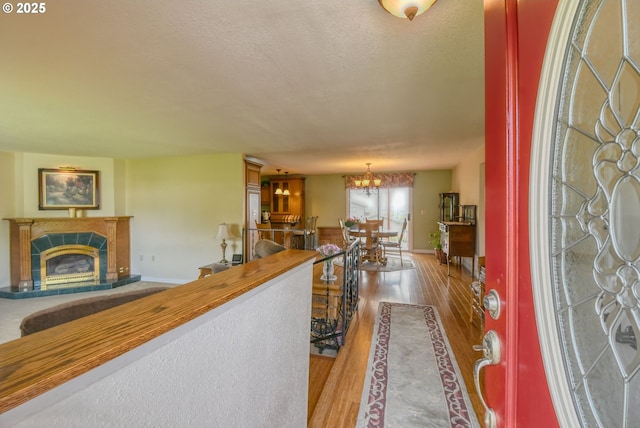entryway with a textured ceiling, a tiled fireplace, wood finished floors, baseboards, and an inviting chandelier