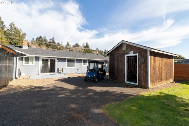 rear view of property featuring a yard, an outdoor structure, and fence