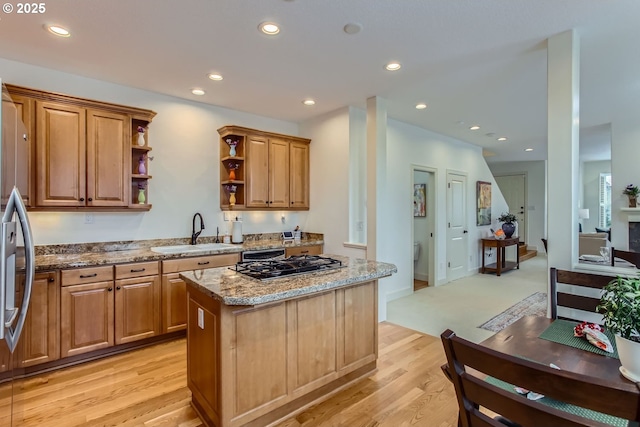 kitchen with sink, a kitchen island, light hardwood / wood-style floors, stainless steel appliances, and light stone countertops