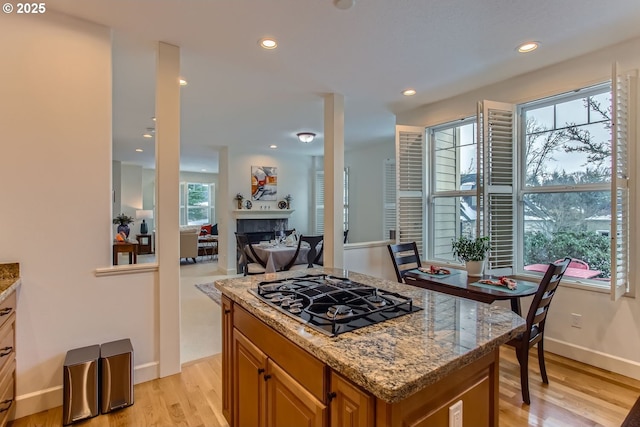 kitchen featuring a fireplace, a center island, light hardwood / wood-style flooring, light stone counters, and gas stovetop