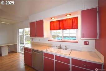 kitchen with light countertops, stainless steel dishwasher, red cabinetry, a sink, and wood finished floors