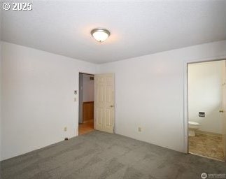 unfurnished bedroom featuring ensuite bathroom and dark colored carpet