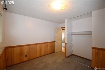 unfurnished bedroom featuring a closet, wainscoting, wooden walls, and carpet flooring