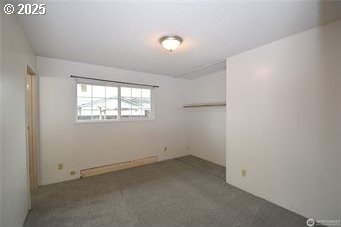 unfurnished room featuring dark colored carpet and baseboard heating