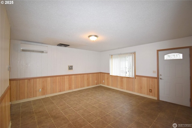 spare room featuring a wainscoted wall, an AC wall unit, a textured ceiling, and wooden walls