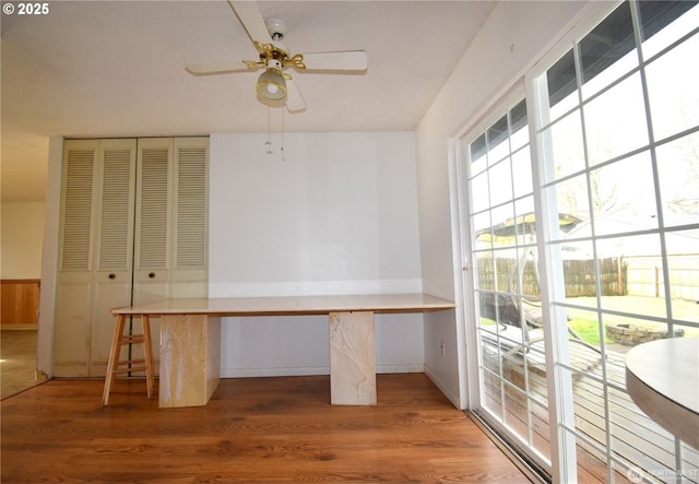 unfurnished office featuring built in desk, a ceiling fan, and wood finished floors