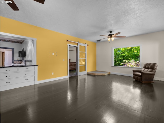 682 S Settlemier Ave, Woodburn, OR 97071 - unfurnished living room with a ceiling fan, a barn door, a textured ceiling, dark wood finished floors, and baseboards