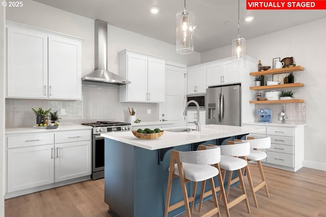 kitchen featuring wall chimney range hood, sink, appliances with stainless steel finishes, white cabinetry, and decorative backsplash