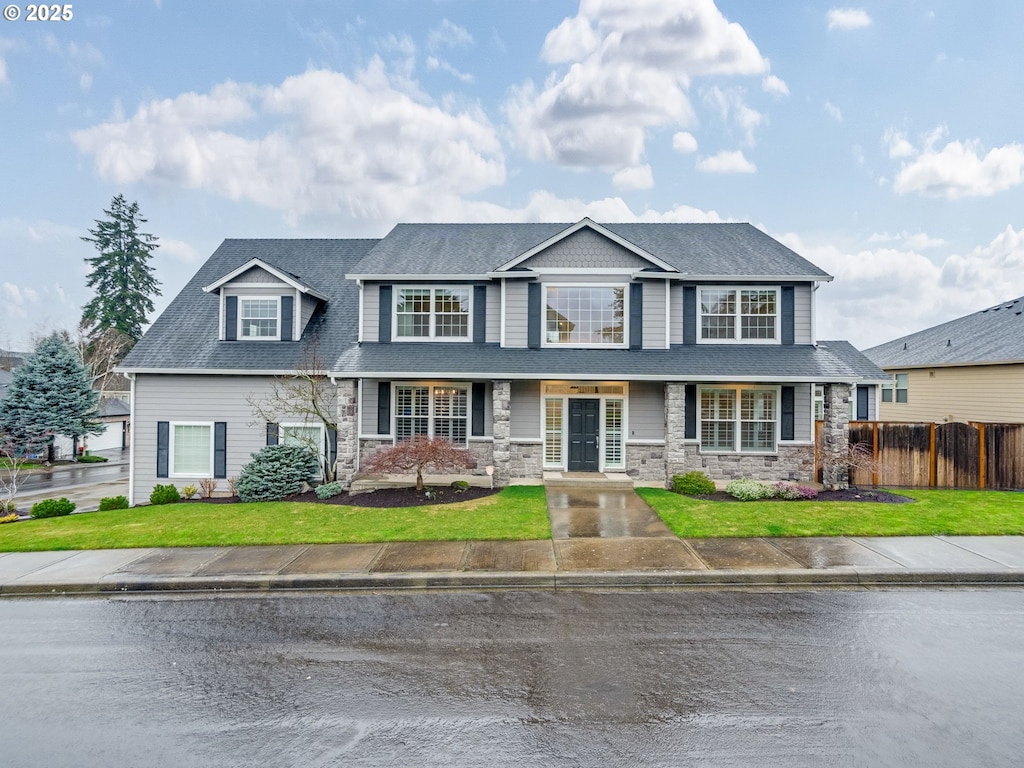 view of front of property featuring stone siding, a shingled roof, a front yard, and fence