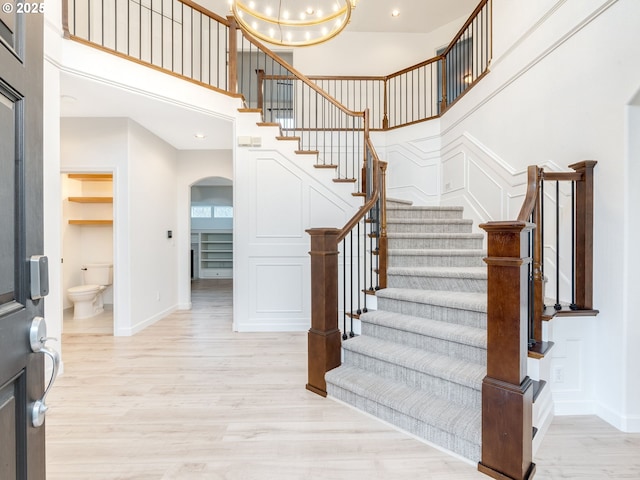 staircase with a high ceiling, wood-type flooring, and a notable chandelier