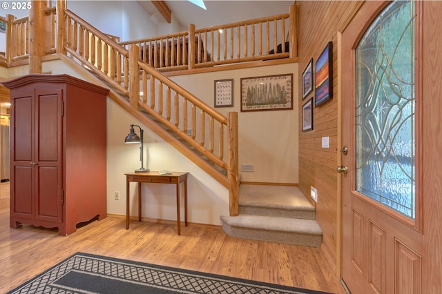 entryway with stairs, light wood finished floors, baseboards, a skylight, and wood walls