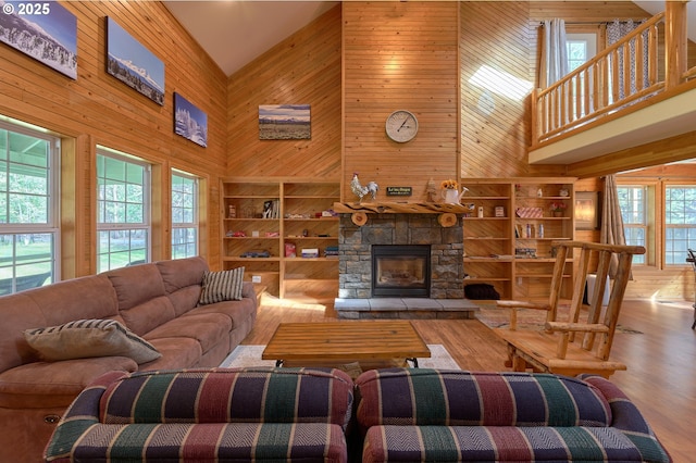 living room featuring high vaulted ceiling, wooden walls, wood finished floors, built in shelves, and a stone fireplace
