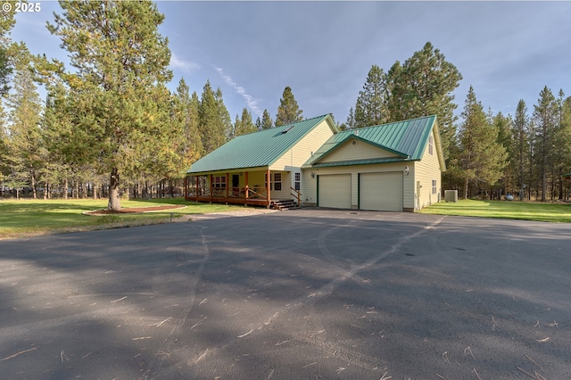 view of front facade featuring asphalt driveway, a garage, a front yard, metal roof, and covered porch