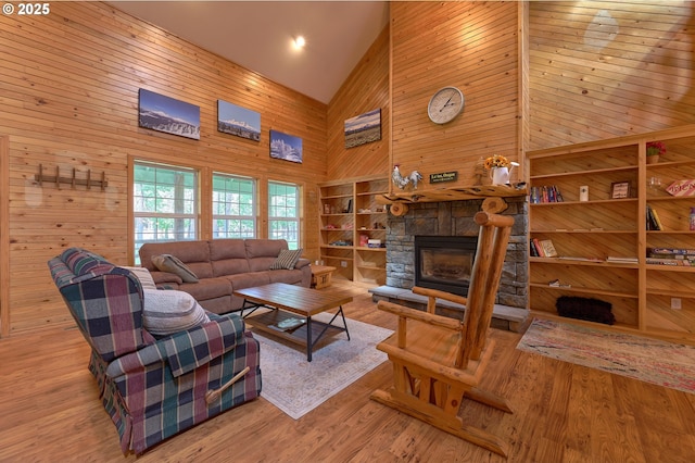 living area with high vaulted ceiling, wooden walls, a fireplace, and wood finished floors