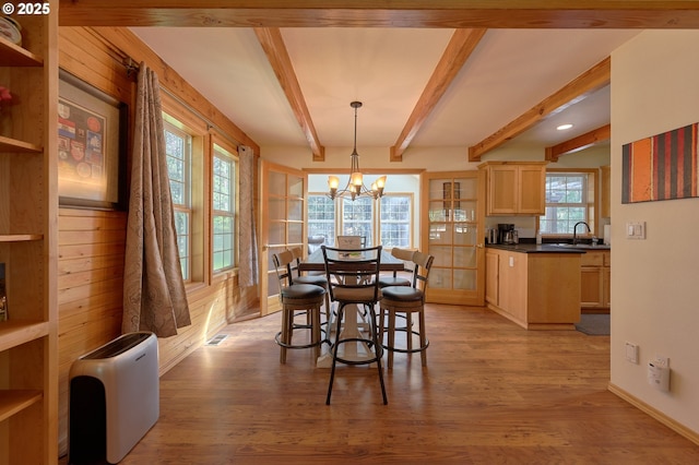 dining area with a chandelier, light wood-style floors, beam ceiling, and baseboards