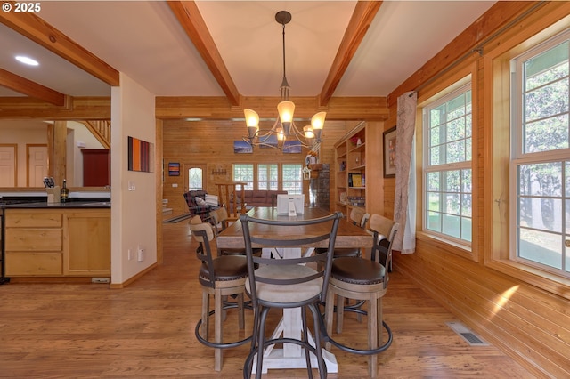 dining space featuring plenty of natural light, wooden walls, light wood finished floors, beamed ceiling, and a chandelier