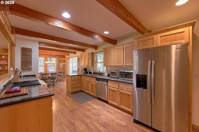 kitchen featuring stainless steel appliances, dark countertops, a sink, light brown cabinetry, and beamed ceiling