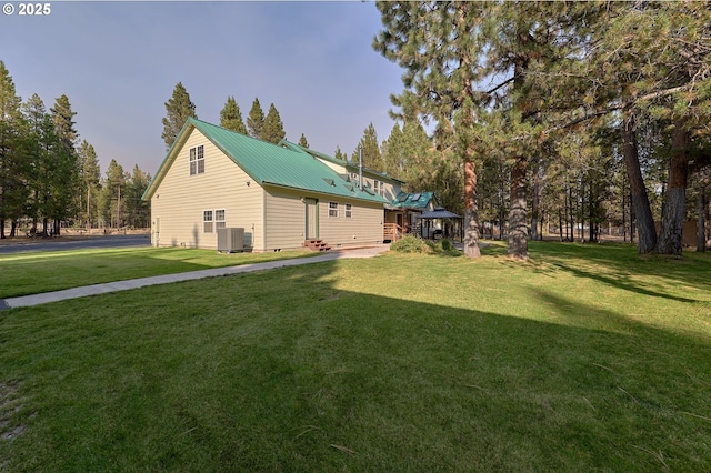 rear view of property with cooling unit, a yard, metal roof, and entry steps