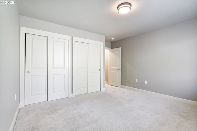 unfurnished bedroom featuring carpet flooring, baseboards, and two closets