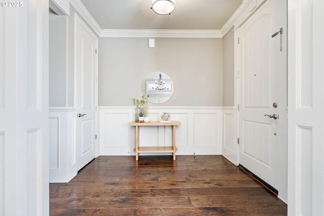 foyer with dark wood finished floors, a decorative wall, an inviting chandelier, ornamental molding, and wainscoting