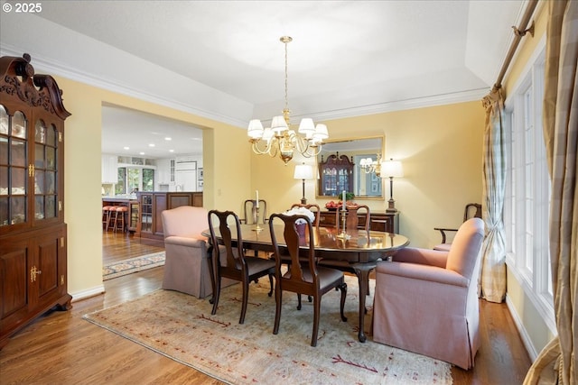 dining space featuring wood-type flooring, ornamental molding, and a chandelier