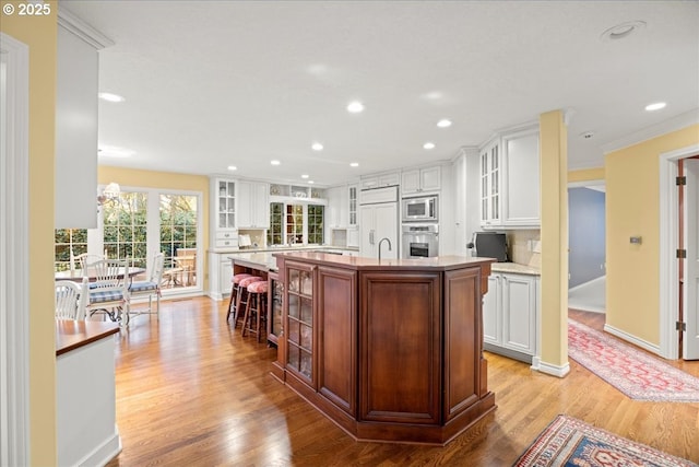 kitchen with white cabinets, a kitchen breakfast bar, built in appliances, an island with sink, and light hardwood / wood-style floors