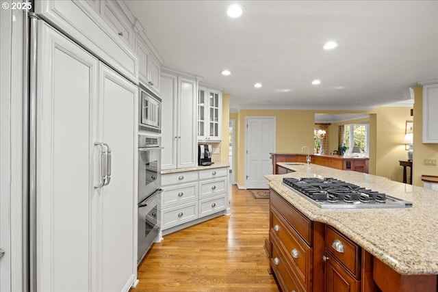 kitchen with white cabinetry, stainless steel appliances, ornamental molding, an island with sink, and light wood-type flooring