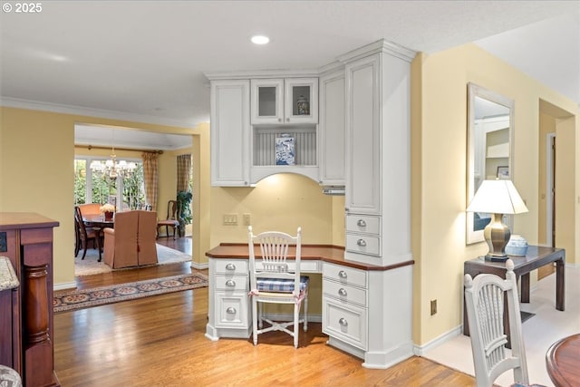 office featuring a notable chandelier, light wood-style flooring, crown molding, baseboards, and built in study area