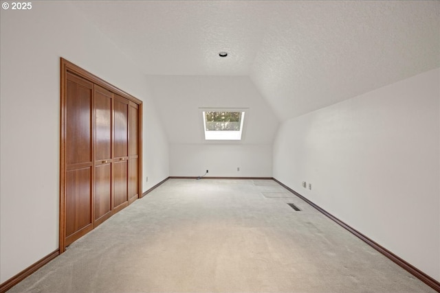 bonus room with a textured ceiling, vaulted ceiling with skylight, and light carpet