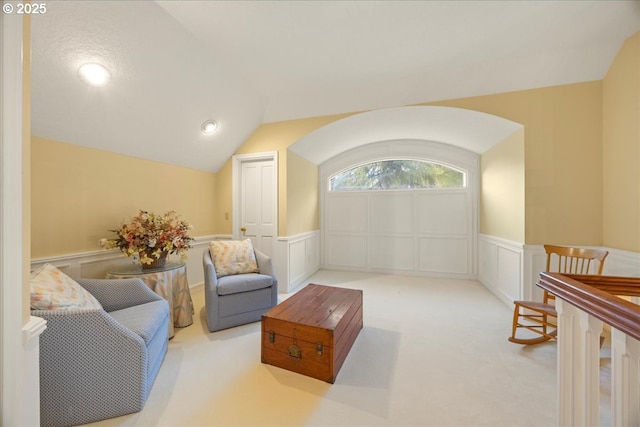 living area featuring a wainscoted wall, carpet floors, arched walkways, and vaulted ceiling