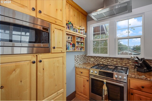 kitchen with light stone counters, appliances with stainless steel finishes, wall chimney range hood, and backsplash