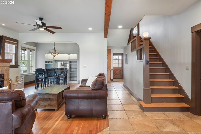 living room with a stone fireplace, a wealth of natural light, and ceiling fan