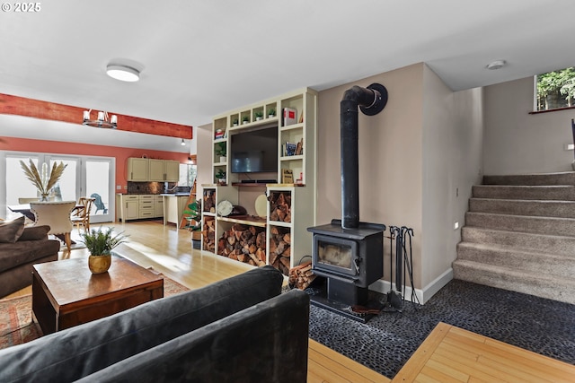 living room with stairway, baseboards, a wood stove, and light wood finished floors