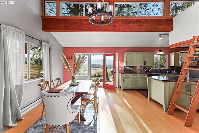 dining area featuring light wood-style flooring, a baseboard heating unit, lofted ceiling with beams, and an inviting chandelier