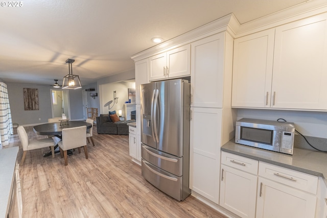 kitchen with stainless steel appliances, white cabinets, light wood-type flooring, and decorative light fixtures