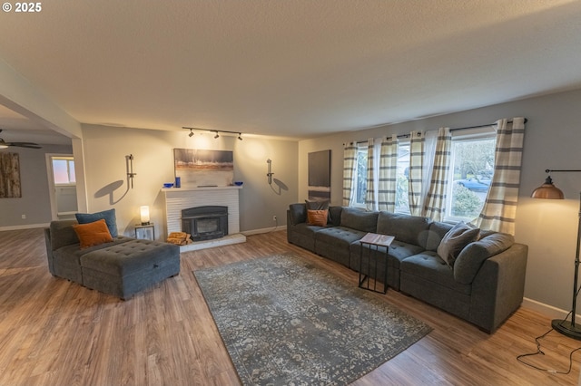 living room featuring a brick fireplace, hardwood / wood-style flooring, a textured ceiling, and ceiling fan