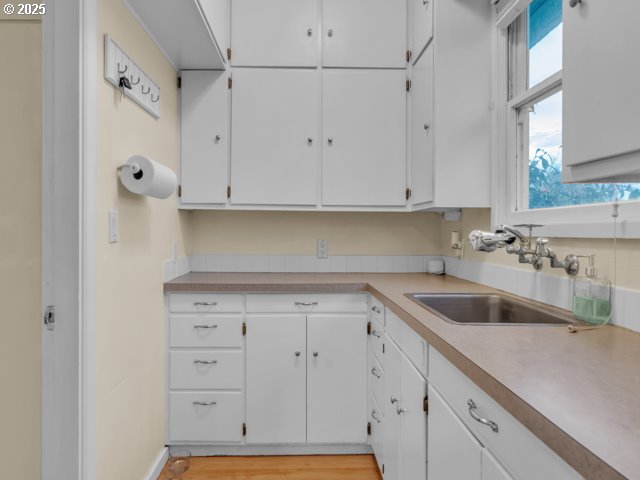 kitchen featuring white cabinetry, light countertops, light wood-type flooring, and a sink