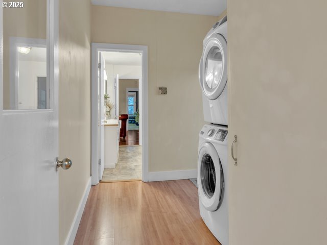 laundry area with baseboards, light wood-style flooring, laundry area, and stacked washing maching and dryer