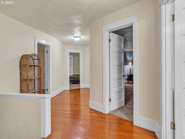 hall featuring baseboards, light wood finished floors, and a textured ceiling