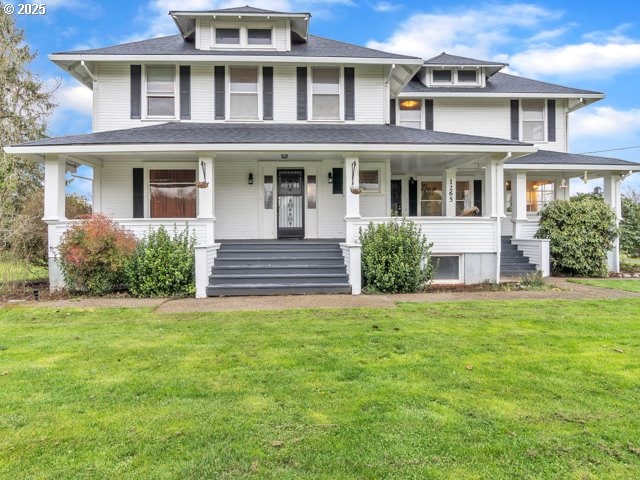 american foursquare style home featuring covered porch, a front yard, and roof with shingles