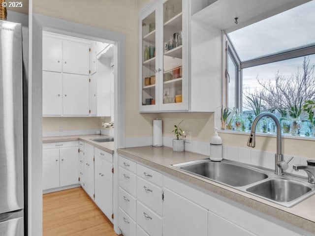 kitchen with freestanding refrigerator, a sink, light countertops, white cabinets, and light wood-style floors