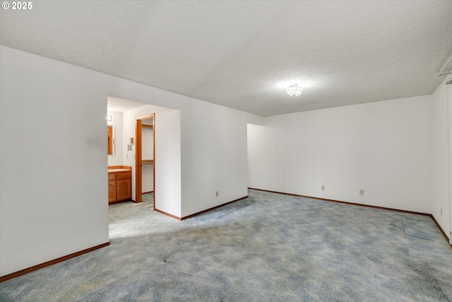 empty room with light colored carpet, baseboards, and a textured ceiling