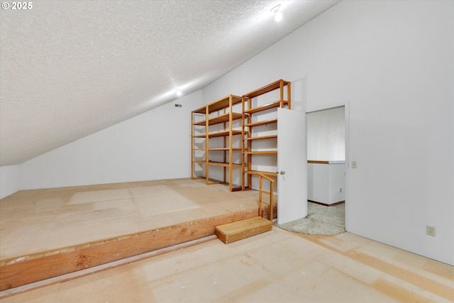 bonus room with a textured ceiling, lofted ceiling, and concrete flooring