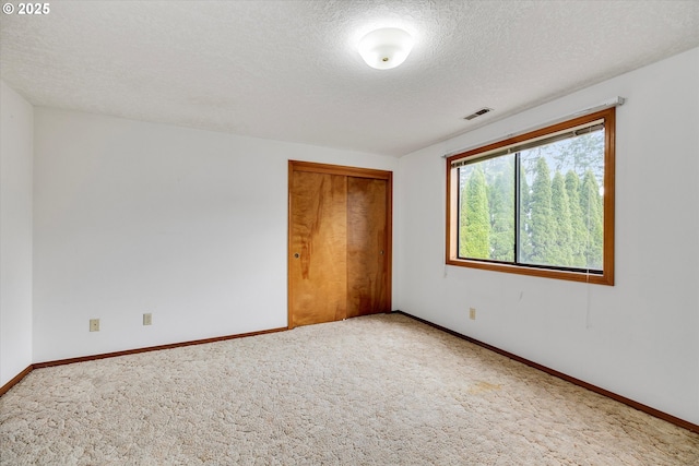 carpeted spare room with a textured ceiling and baseboards