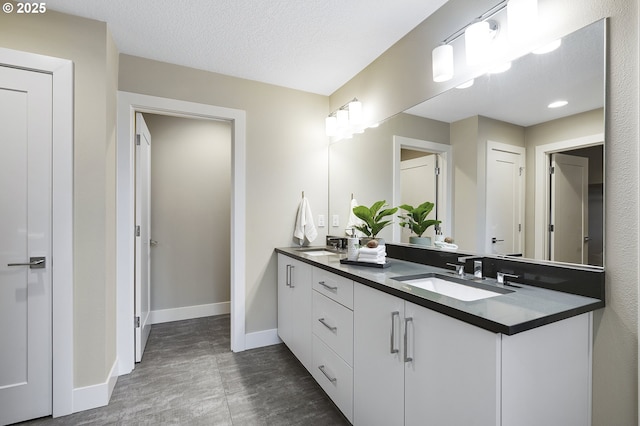 bathroom featuring double vanity, a textured ceiling, baseboards, and a sink