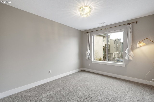 carpeted spare room with baseboards, visible vents, and a textured ceiling