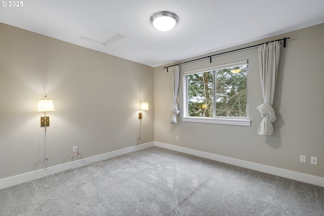 unfurnished room featuring a textured ceiling, carpet, attic access, and baseboards